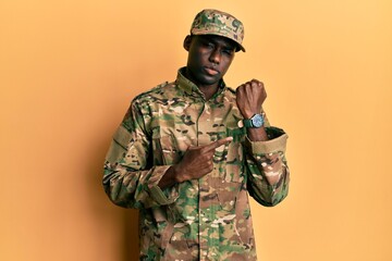Young african american man wearing army uniform in hurry pointing to watch time, impatience,...