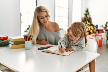 Fototapeta premium Mother and daughter drawing on notebook sitting by christmas tree at home