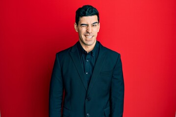 Obraz premium Handsome hispanic man wearing business clothes winking looking at the camera with sexy expression, cheerful and happy face.