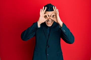Handsome hispanic man wearing business clothes doing ok gesture like binoculars sticking tongue out, eyes looking through fingers. crazy expression.