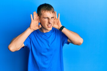 Young caucasian man wearing casual blue t shirt trying to hear both hands on ear gesture, curious for gossip. hearing problem, deaf