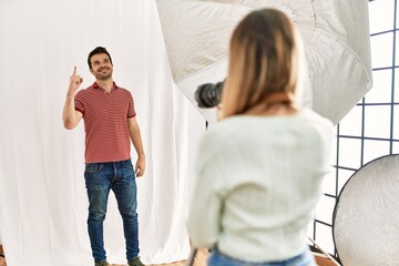 Fototapeta premium Woman photographer talking pictures of man posing as model at photography studio pointing finger up with successful idea. exited and happy. number one.