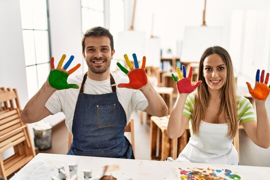 Two hispanic students smiling happy showing colorulf painted hands at art studio.