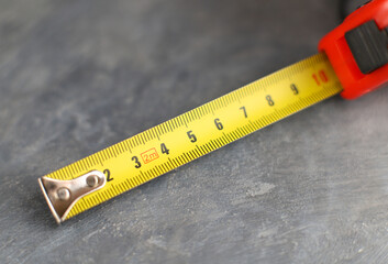 Construction measuring tape on gray concrete background, close-up