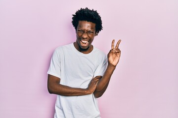 Young african american man wearing casual white t shirt smiling with happy face winking at the...