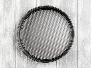 Empty round metal form for baking with removable bumpers on gray wooden background