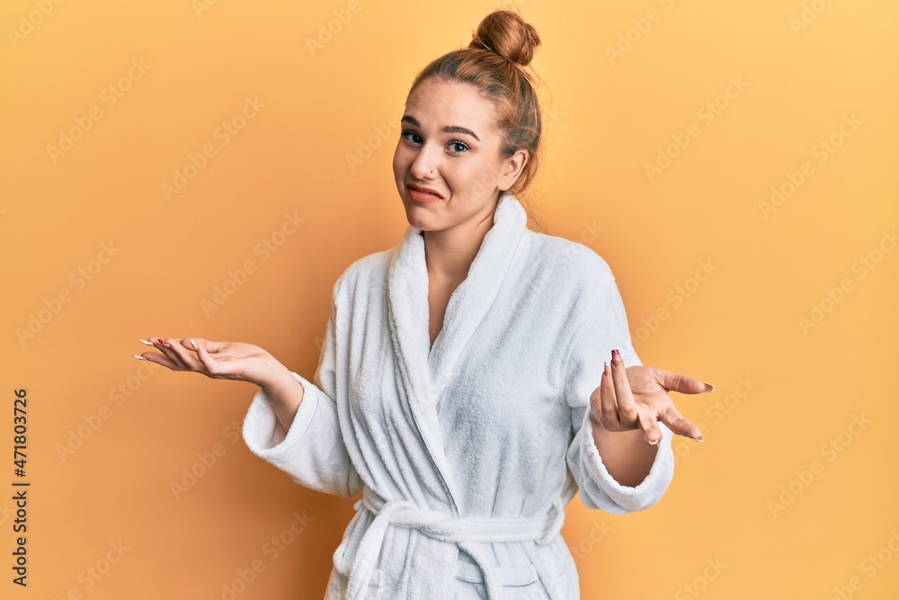 Sticker young blonde woman wearing bathrobe clueless and confused expression with arms and hands raised. dou