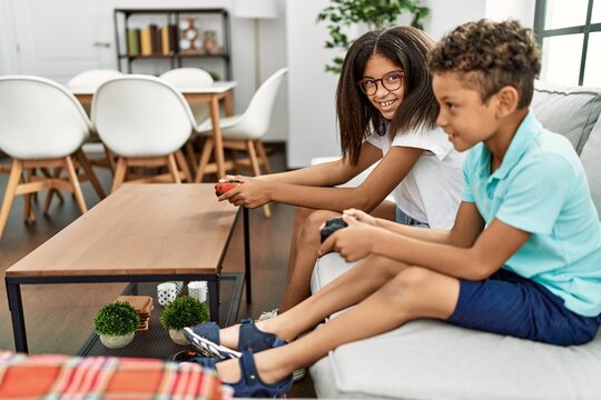 Brother and sister playing video game sitting on sofa at home
