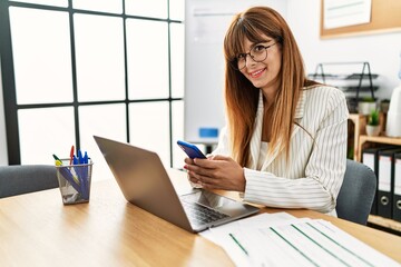 Young hispanic businesswoman working using smartphone and laptop at the office.