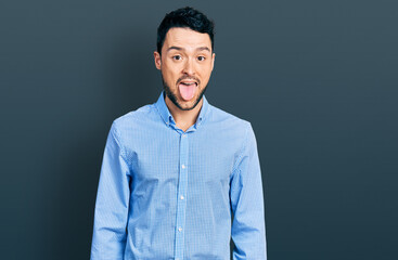 Hispanic man with beard wearing casual business shirt sticking tongue out happy with funny expression. emotion concept.