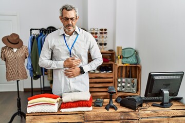 Middle age hispanic man working as manager at retail boutique with hand on stomach because indigestion, painful illness feeling unwell. ache concept.