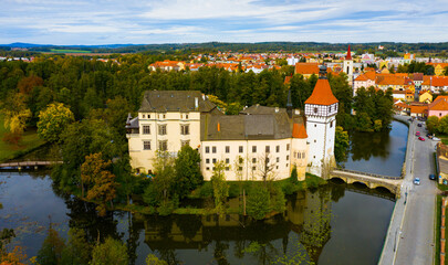 Fototapeta na wymiar Aerial view of medieval Blatna water castle surrounded parks and lakes on background with cityscape on autumn day, South Bohemian Region, Czech Republic..