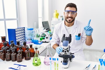 Handsome hispanic man working at scientist laboratory smiling happy pointing with hand and finger...