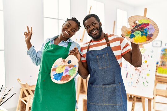 African american painter couple smiling happy holding paintbrush and palette at art studio.