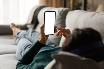 Female using phone. Over shoulder view of young woman lying on sofa hold smartphone with blank...