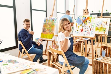 Group of middle age artist at art studio pointing to the back behind with hand and thumbs up, smiling confident
