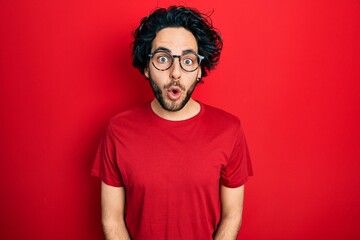 Handsome hispanic man wearing casual t shirt and glasses afraid and shocked with surprise expression, fear and excited face.