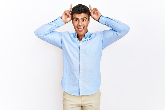 Young hispanic man wearing business shirt standing over isolated background posing funny and crazy with fingers on head as bunny ears, smiling cheerful