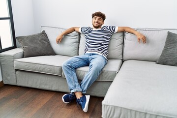 Fototapeta premium Young arab man smiling confident sitting on the sofa at home