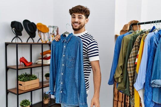 Young arab man customer holding shirt shopping at clothing store