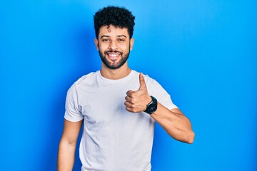 Young arab man with beard wearing casual white t shirt doing happy thumbs up gesture with hand. approving expression looking at the camera showing success.
