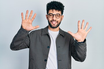 Young arab man with beard wearing glasses showing and pointing up with fingers number ten while smiling confident and happy.