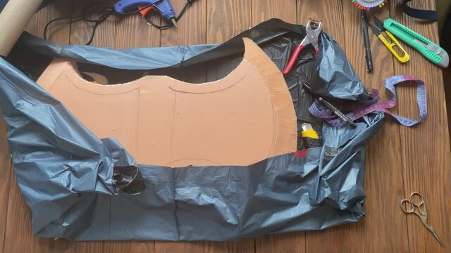 Women's hands spread garbage bag on wooden table and show styrofoam Celtic axe. Viking hatchet for medieval fighting festival. Workshop of cosplayer. Diy craft made of foamed polyethylene.