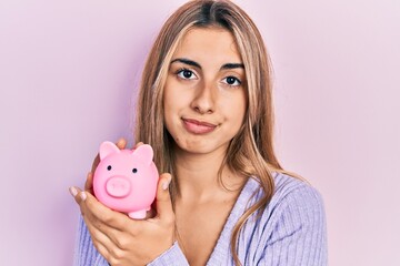 Fototapeta na wymiar Beautiful hispanic woman holding piggy bank relaxed with serious expression on face. simple and natural looking at the camera.