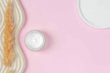 Open jar of cream on pink background with geometric shapes and place for text