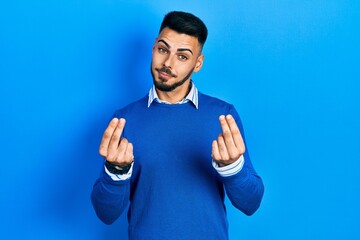 Young hispanic man with beard wearing casual blue sweater doing money gesture with hands, asking...