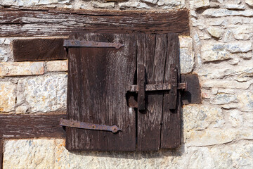 Piccola antica finestra completamente in legno caratteristica delle vecchie abitazioni di montaga su facciata di muro costruito in pietra e mattoncino.