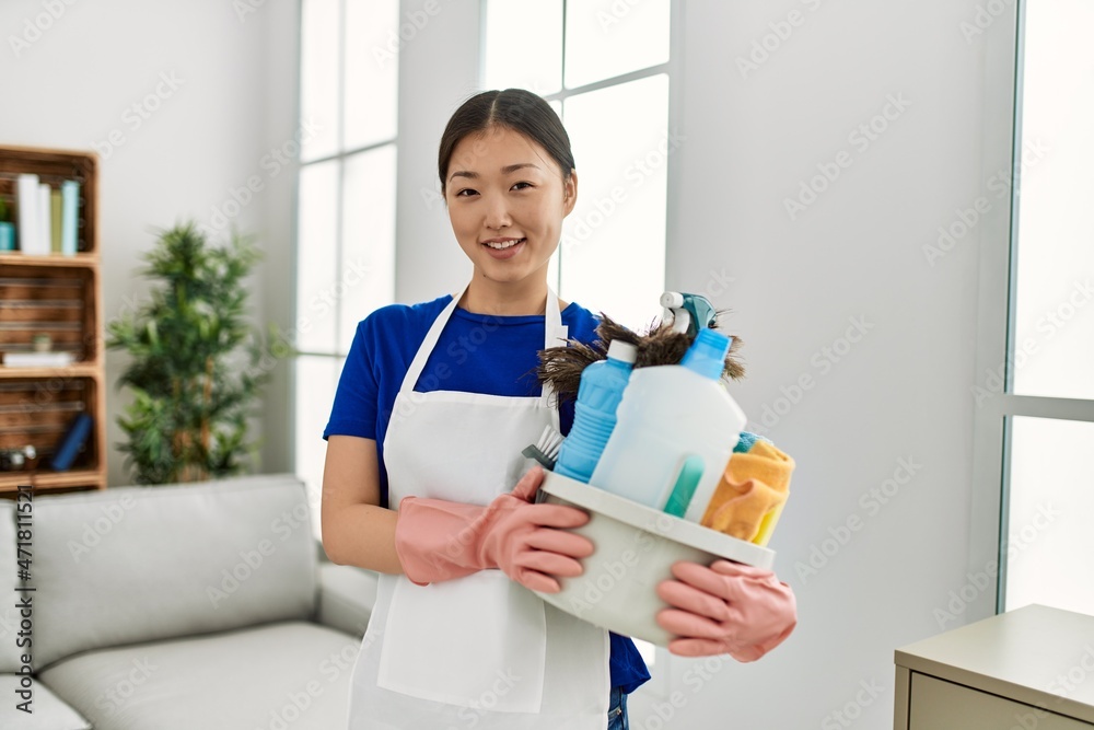 Wall mural young chinese housewife holding cleaning products standing at home. - Wall murals