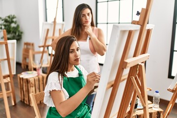 Student and teacher with serious expression painting at art school.