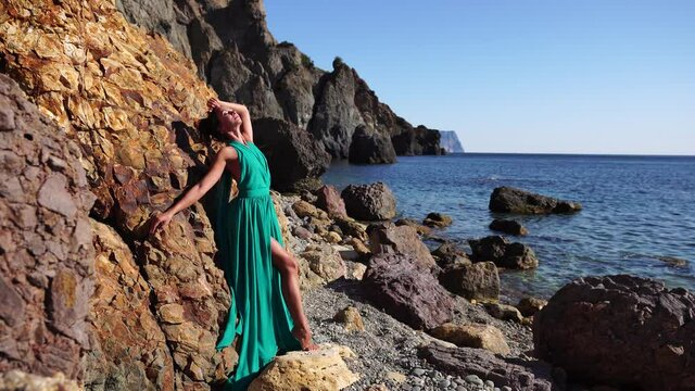 Side view a Young beautiful sensual woman with black hair in a long mint dress posing on a beach with calm sea bokeh lights on sunny day. Girl on the nature on blue sky background. Fashion photo