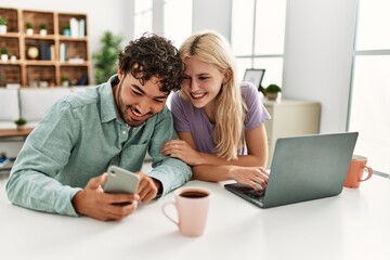 Young couple using laptop and smartphone drinking coffee at home.