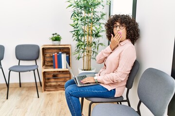 Young middle eastern woman sitting at waiting room working with laptop covering mouth with hand, shocked and afraid for mistake. surprised expression