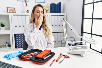 Young beautiful doctor woman with reflex hammer and medical instruments bored yawning tired covering mouth with hand. restless and sleepiness.