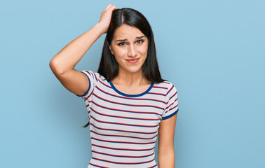 Young hispanic girl wearing casual striped t shirt confuse and wonder about question. uncertain with doubt, thinking with hand on head. pensive concept.