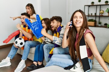 Obraz premium Group of young friends watching and supporting soccer match. Woman talking on the smartphone at home.