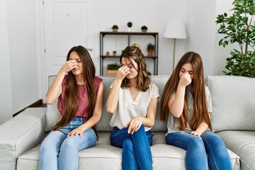 Group of three hispanic girls sitting on the sofa at home tired rubbing nose and eyes feeling fatigue and headache. stress and frustration concept.