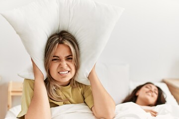 Girl covering ears with pillow irritated for snore lying in bed at home.