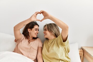 Young couple smiling happy doing heart symbol with hands at bedroom.