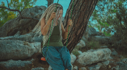 Rasta girl with dreadlocks is resting on the Mediterranean coast on a swing