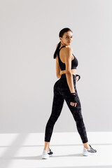 Obraz premium Rear view of fit fitness woman in leggings, turn head at camera with confident face expression, standing over white background