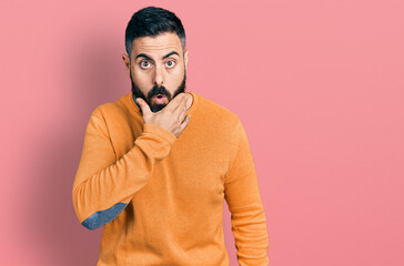 Hispanic man with beard wearing casual winter sweater looking fascinated with disbelief, surprise and amazed expression with hands on chin