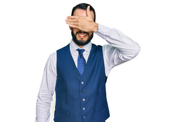 Young man with beard wearing business vest smiling and laughing with hand on face covering eyes for surprise. blind concept.