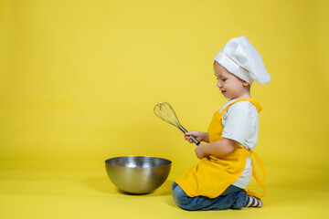 Boy in apron and chef's hat sitting on the floor with a bowl and whisk