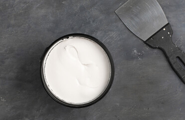 Construction spatula and white acrylic putty on gray concrete background