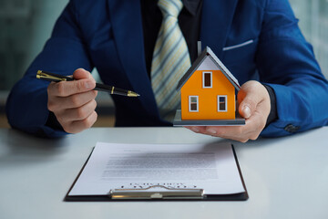 A real estate agent offers a sample home insurance home to sign the agreement. with documents of...