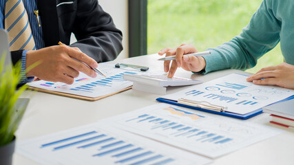 Business team discussing and planning projects using charts, holding pens and analytical papers on office table. with a laptop computer and a financial graph running in the background. business idea